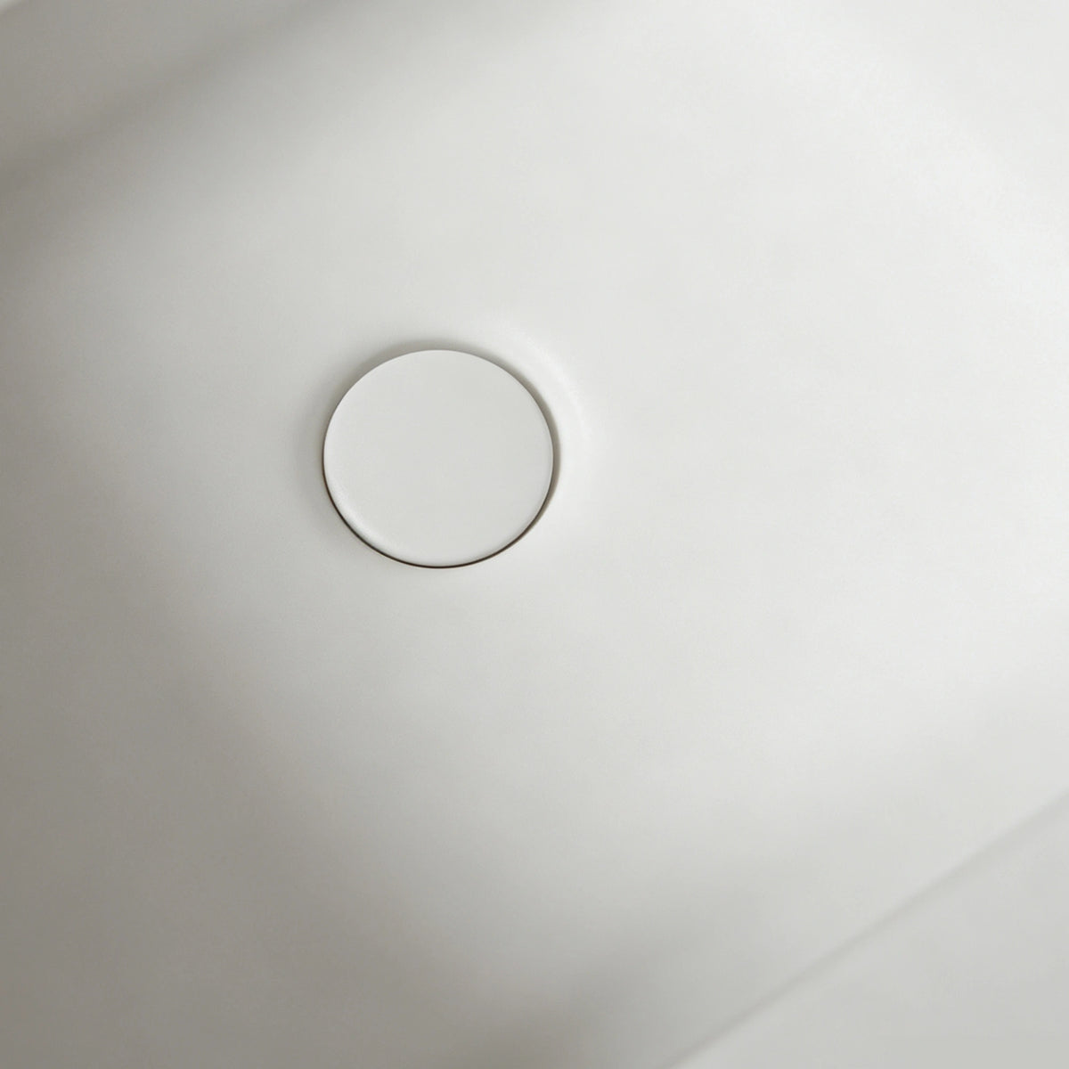 Close-up of the color-matched drain inside the matte white bathtub.
