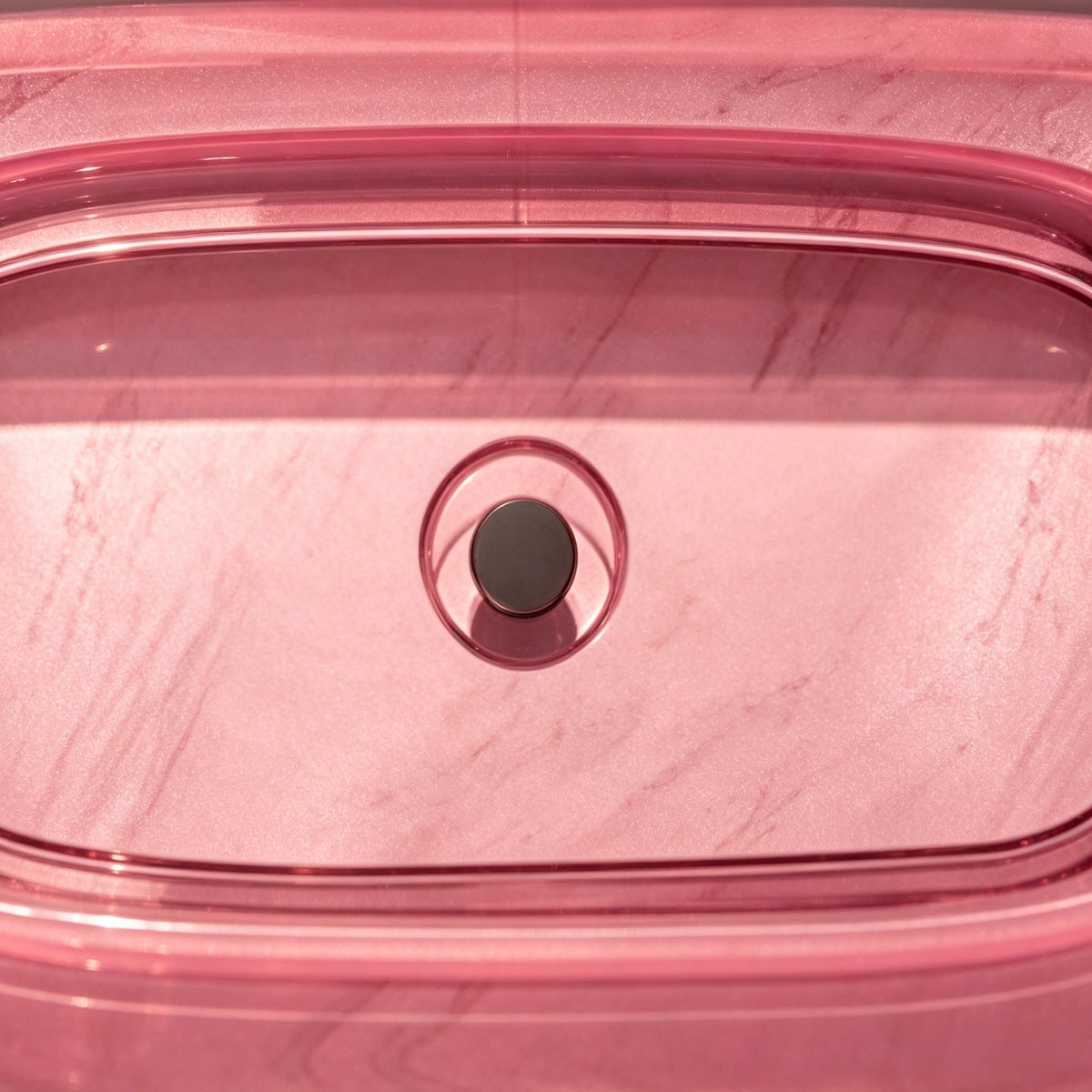 Close-up of the dark overflow fitting inside the pink resin bathtub.