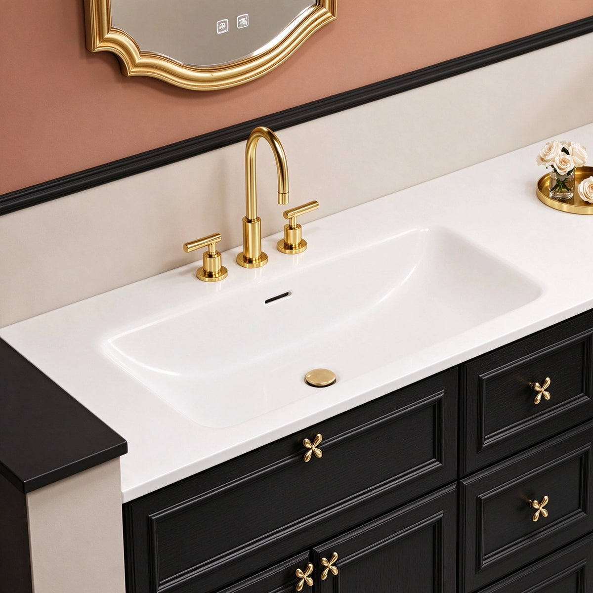 Partial view of sink and cabinet, long undermount white sink, 3‑handle gold faucet, ornate gold pulls, recessed‑line cabinet panel