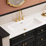 Partial view of sink and cabinet, long undermount white sink, 3‑handle gold faucet, ornate gold pulls, recessed‑line cabinet panel