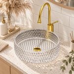 Round diamond-cut clear glass vessel sink paired with gold faucet on speckled countertop in warm modern bathroom setting