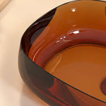 Close-up of the curved basin edge and glossy orange-red resin surface on an oval vessel bathroom sink