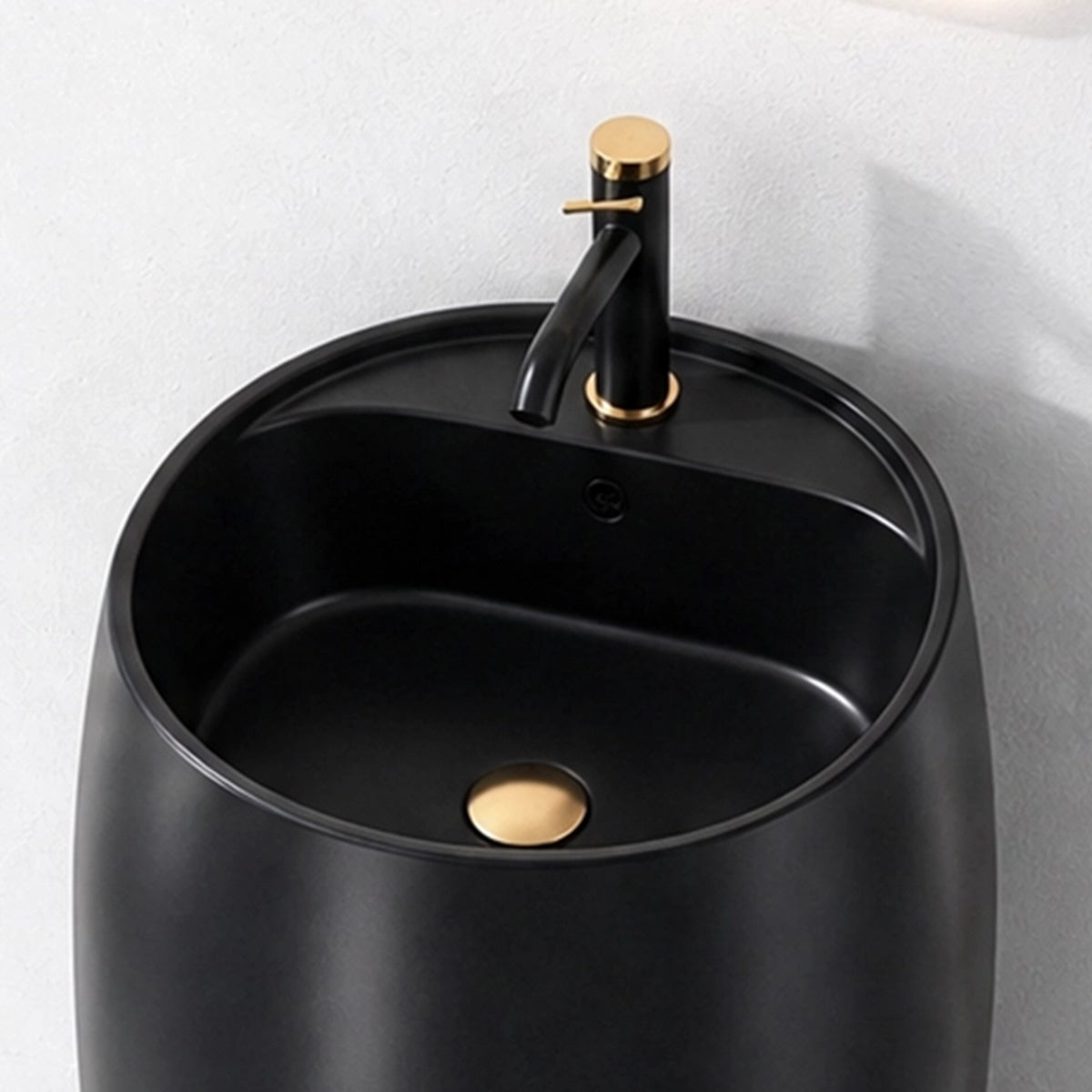 Close-up of black ceramic round pedestal bathroom sink with black and gold faucet and integrated overflow