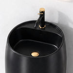 Close-up of black ceramic round pedestal bathroom sink with black and gold faucet and integrated overflow