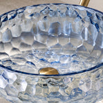 Blue glass round vessel bathroom sink with textured glass surface and visible drain opening