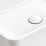 Close-up of the white ceramic semi-recessed bathroom sink featuring a smooth basin surface and a round white drain cover with a chrome rim.