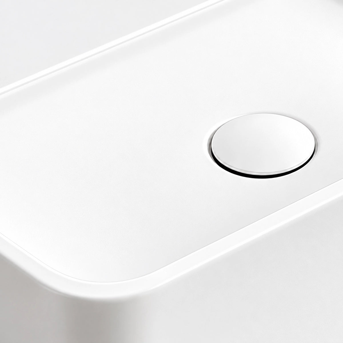 Close-up of the white ceramic semi-recessed bathroom sink featuring a smooth basin surface and a round white drain cover with a chrome rim.